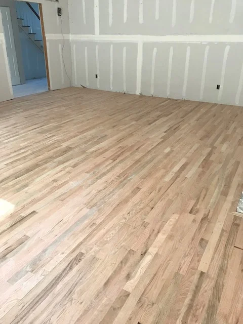 Light oak hardwood flooring installed in diagonal pattern with white drywall walls and blue doorway