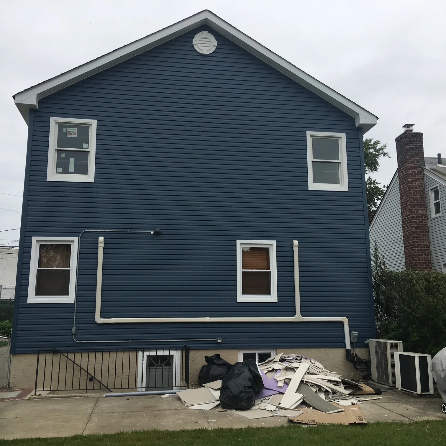 Navy blue vinyl siding with white-trimmed windows and new metal basement railing on two-story home