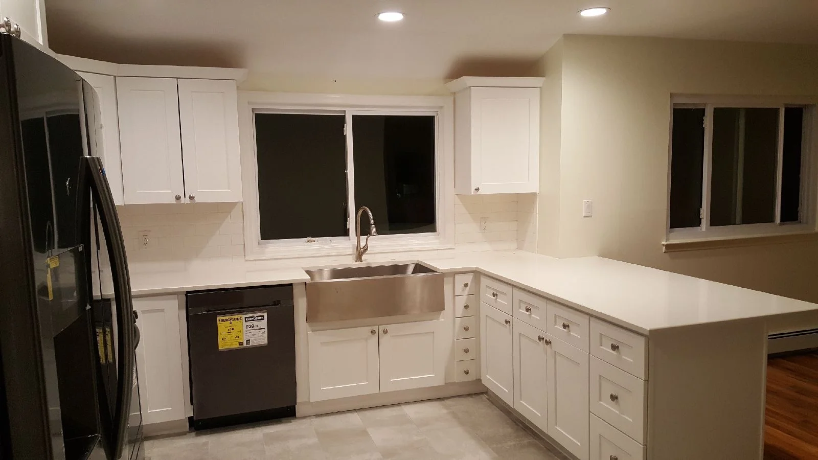 White kitchen cabinets, quartz countertops, stainless steel sink, black appliances, recessed lighting