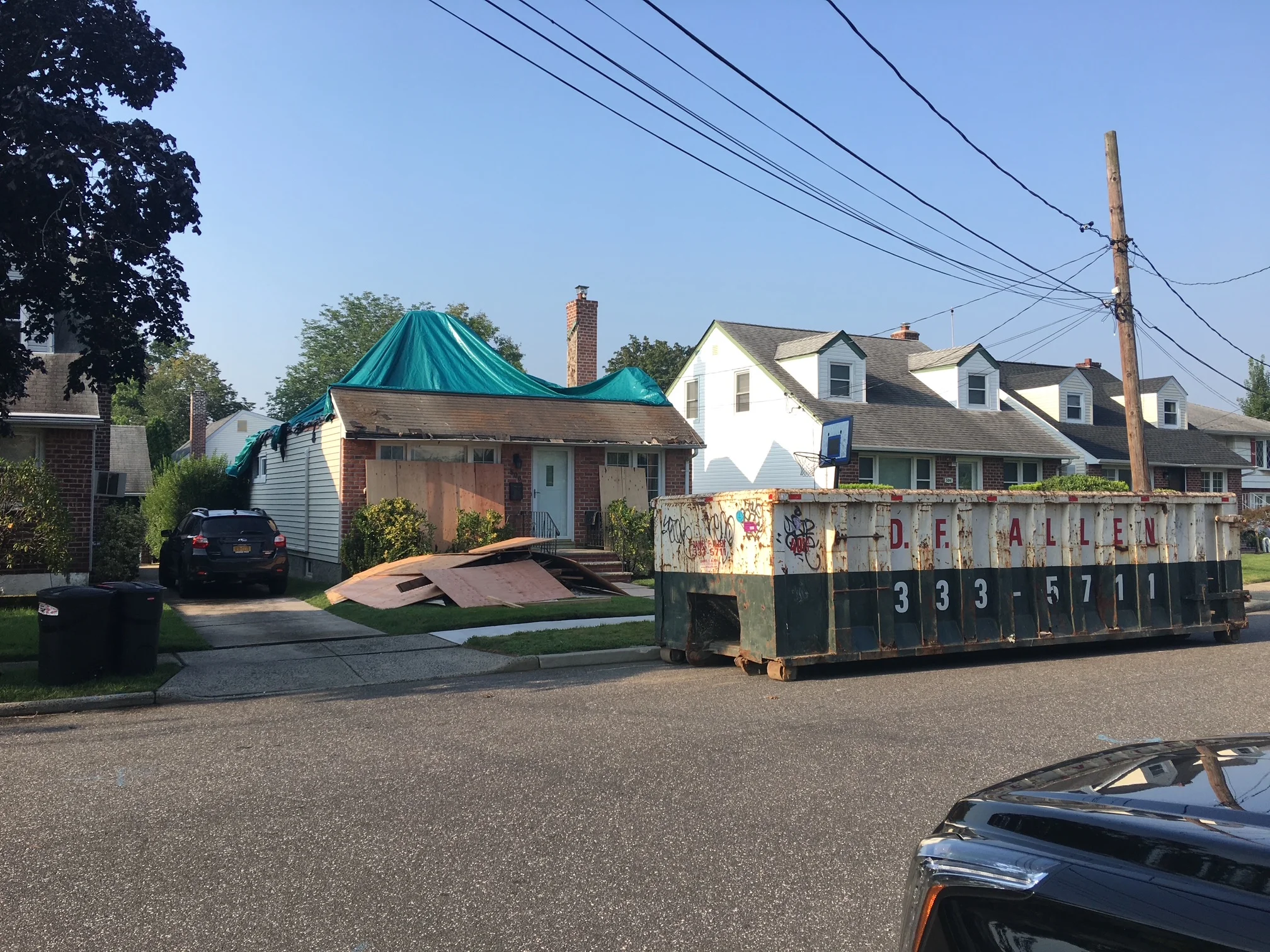 Residential roof replacement with teal metal roof, brick chimney, and dumpster on driveway