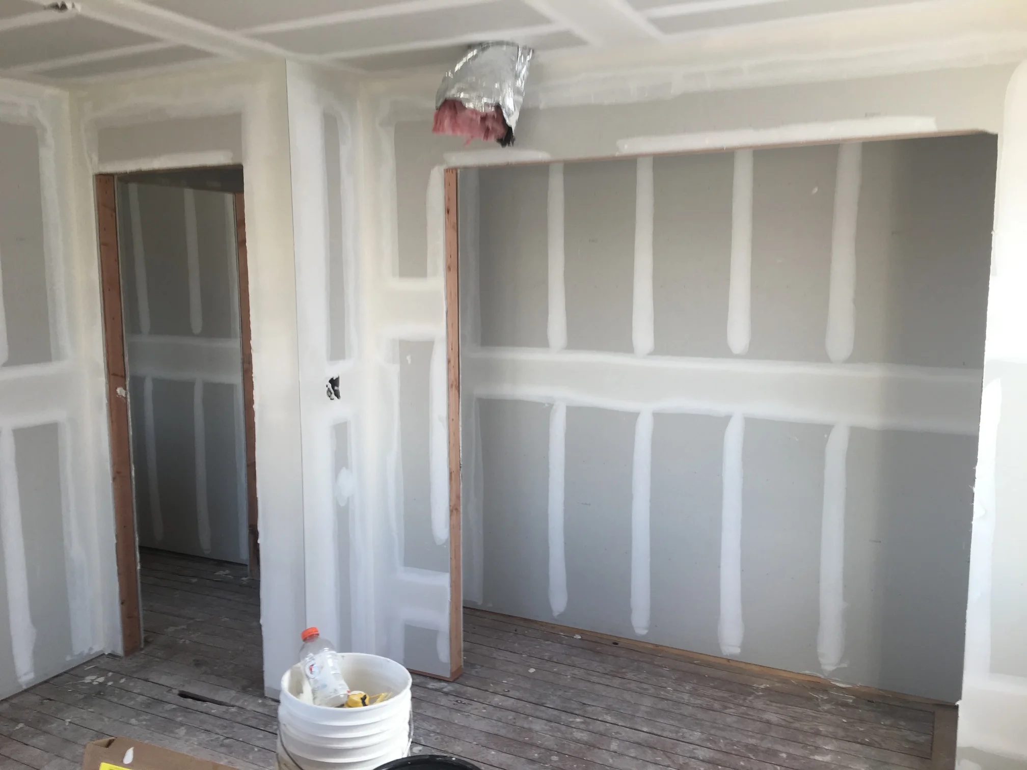 Drywall installation with metal studs, white sheets, and taped seams in interior room