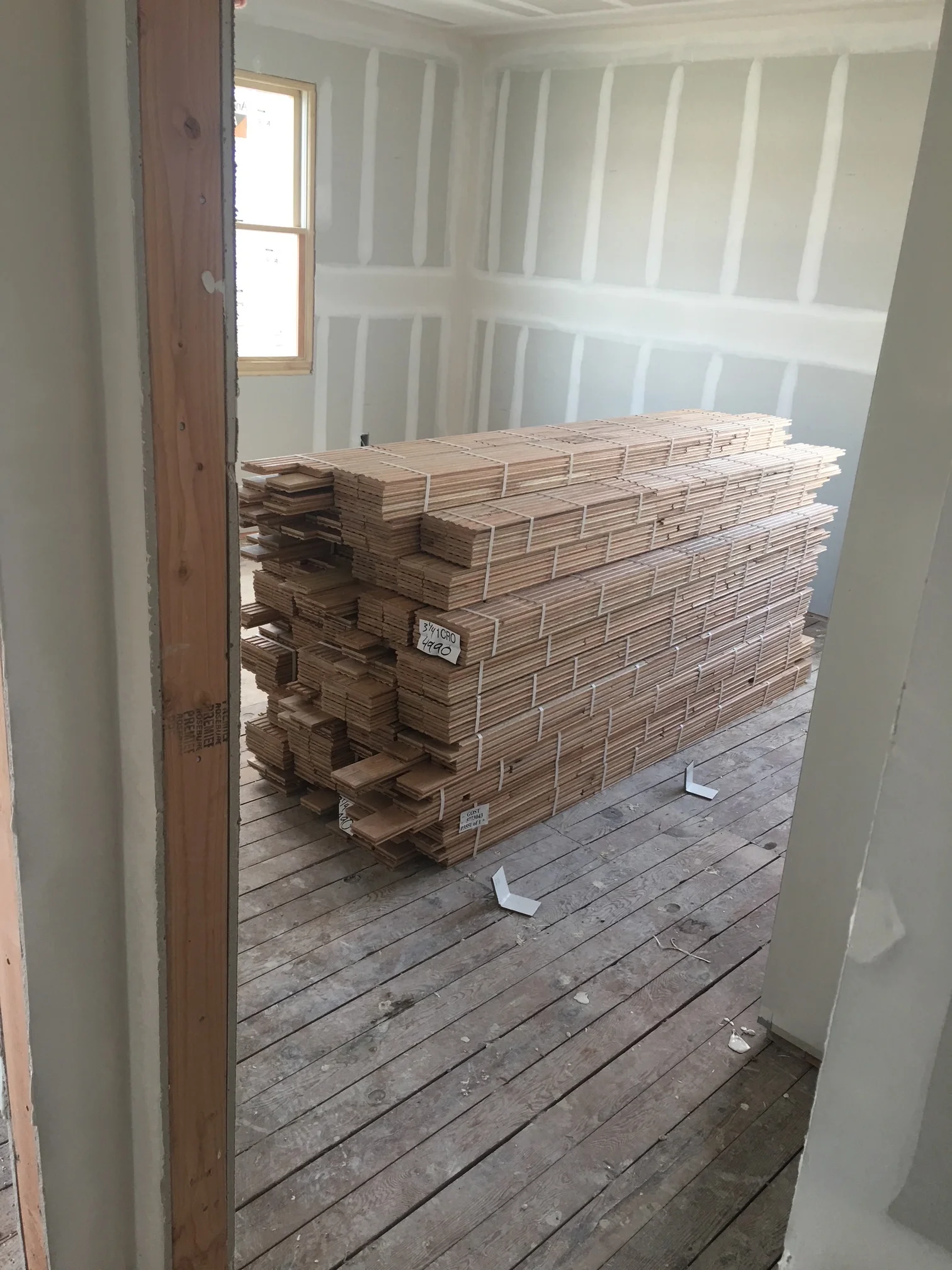Drywall-framed room with stacked engineered hardwood flooring bundles staged for installation
