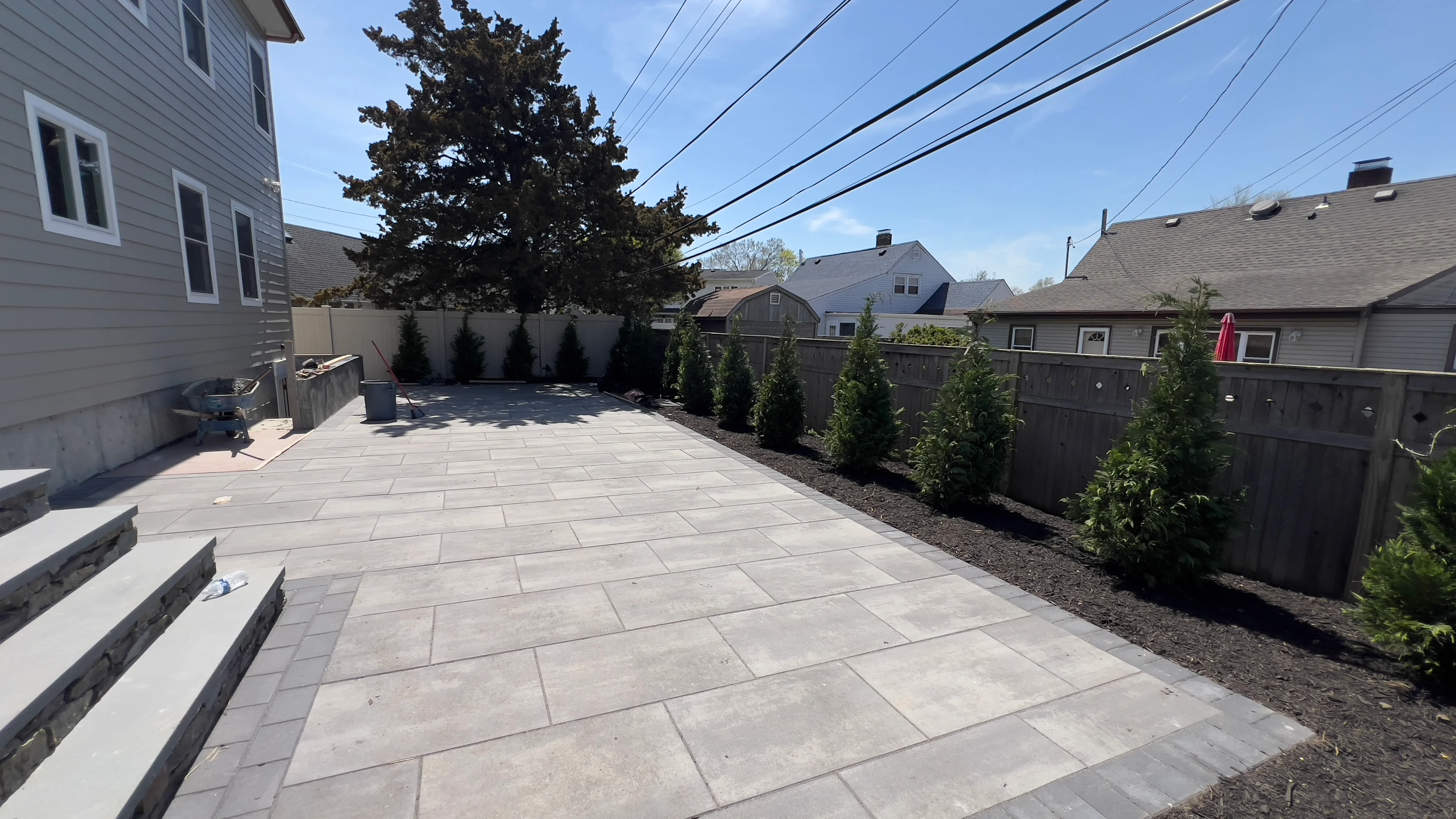 Gray concrete paver patio with evergreen plantings and mulch borders along wooden fence
