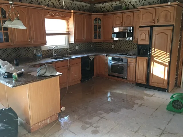 Water-damaged kitchen with wet flooring, wood cabinetry, and tile backsplash requiring restoration