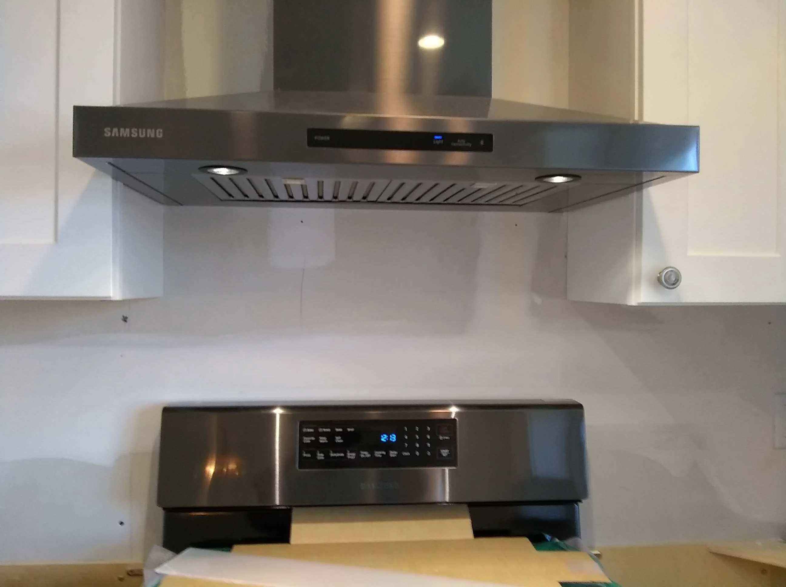 Stainless steel Samsung range hood and dishwasher installed in white kitchen cabinetry