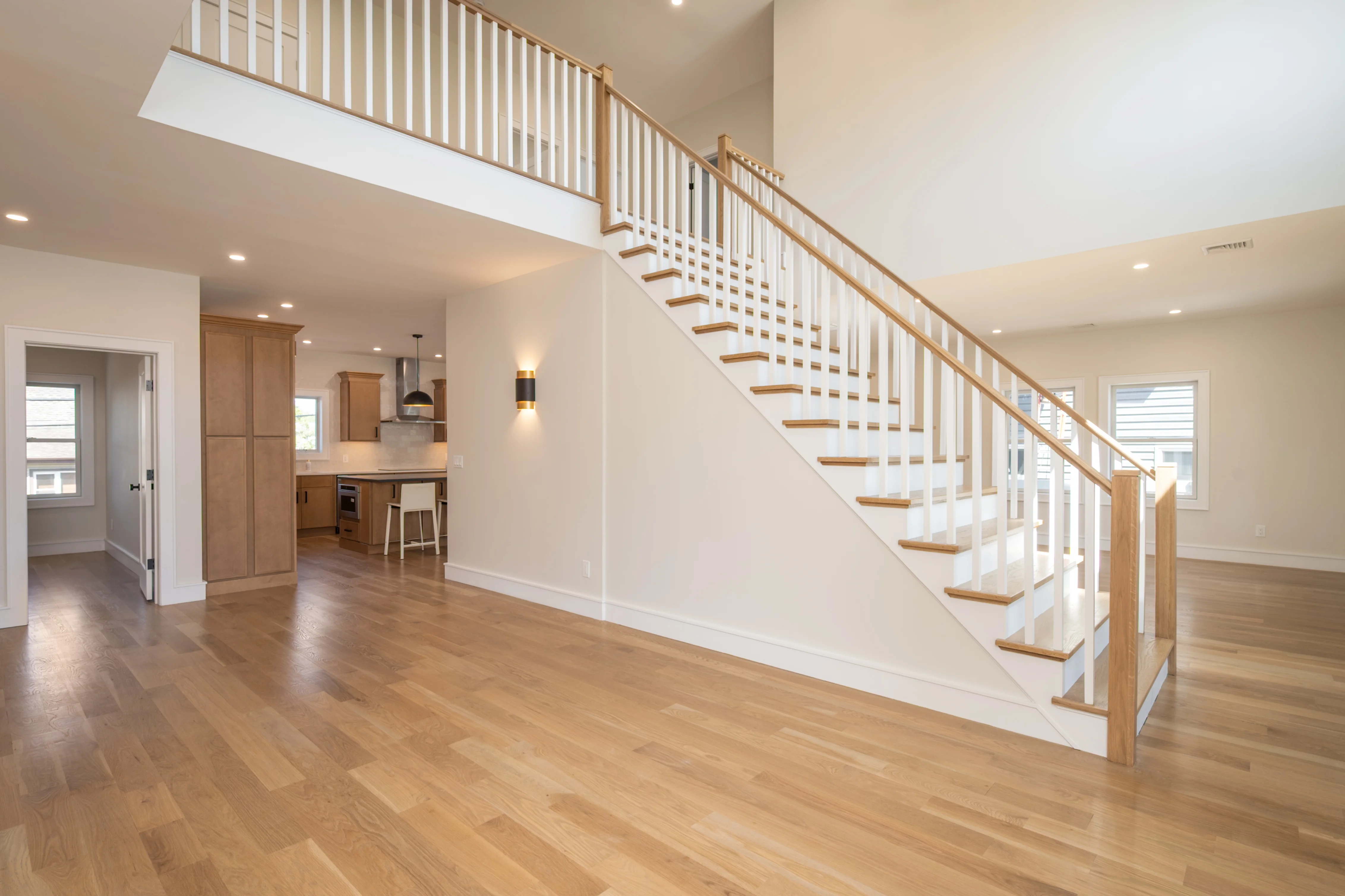 Open-concept interior with custom wood staircase, oak treads, white balusters, and engineered hardwood flooring