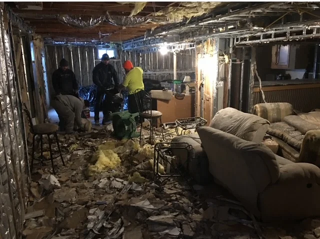 Basement interior demolition showing exposed framing, removed drywall, and debris removal after fire and water damage