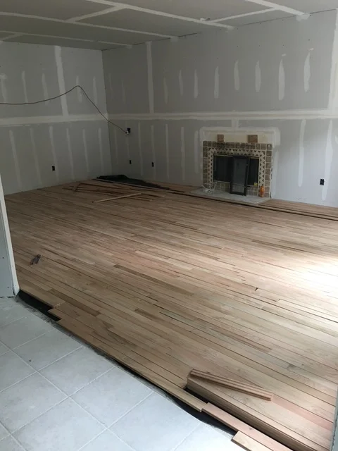 Drywall-taped walls and ceiling with new hardwood flooring installation in open room with fireplace
