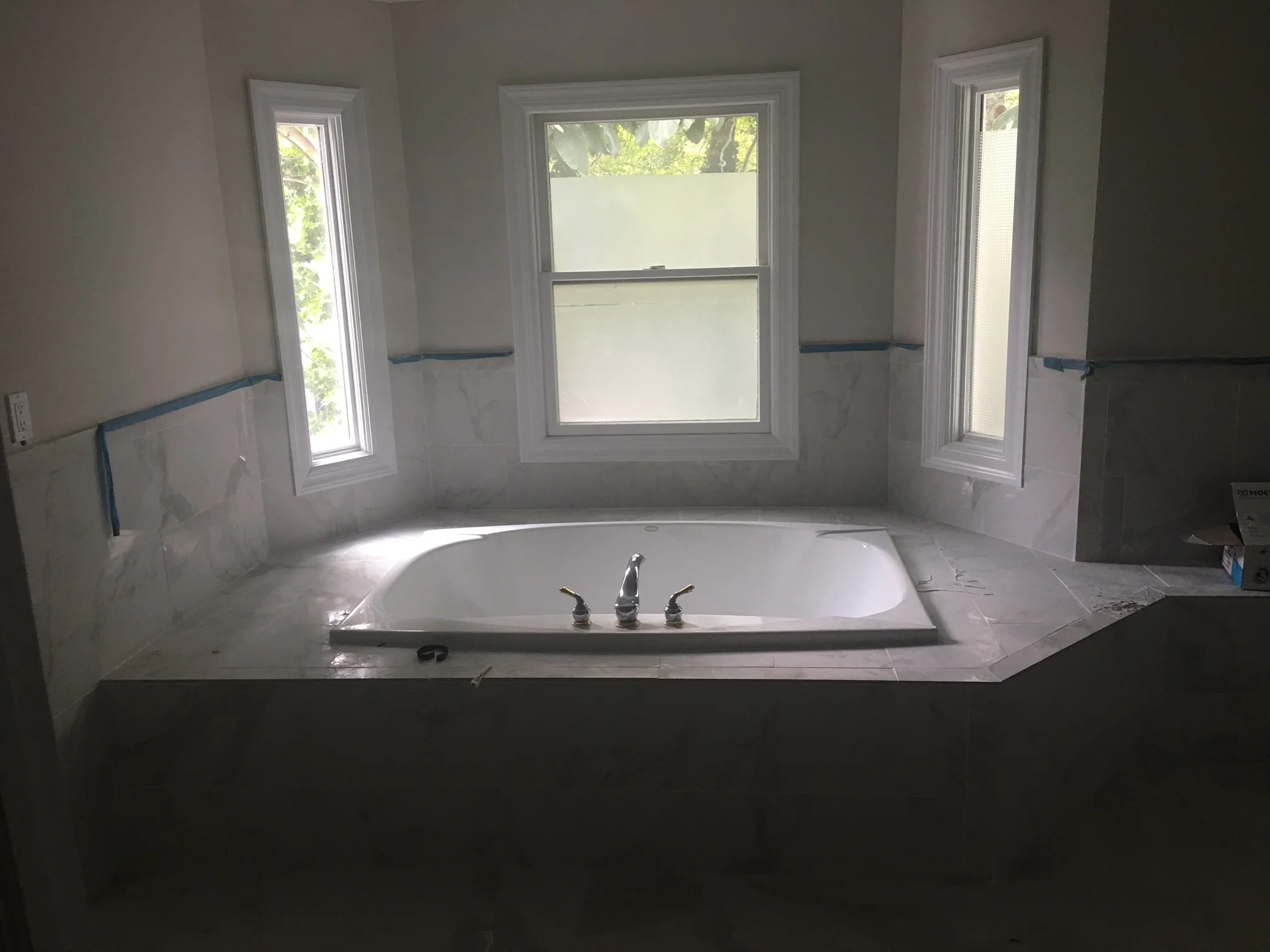 Drop-in soaking tub with chrome faucet, white drywall, and three windows in renovated master bathroom
