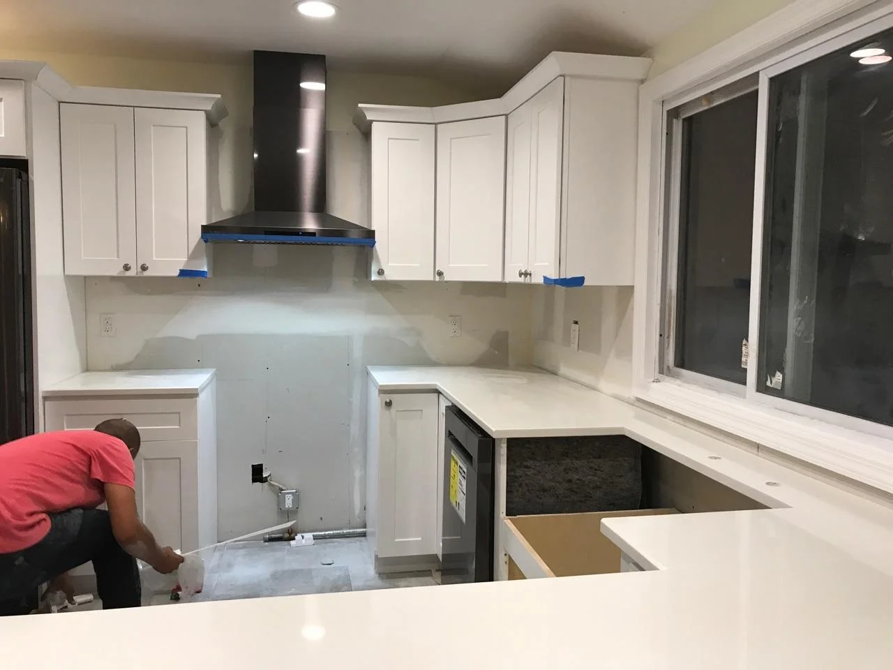 Kitchen renovation with white cabinetry, quartz counters, stainless steel hood, and drywall finishing in progress