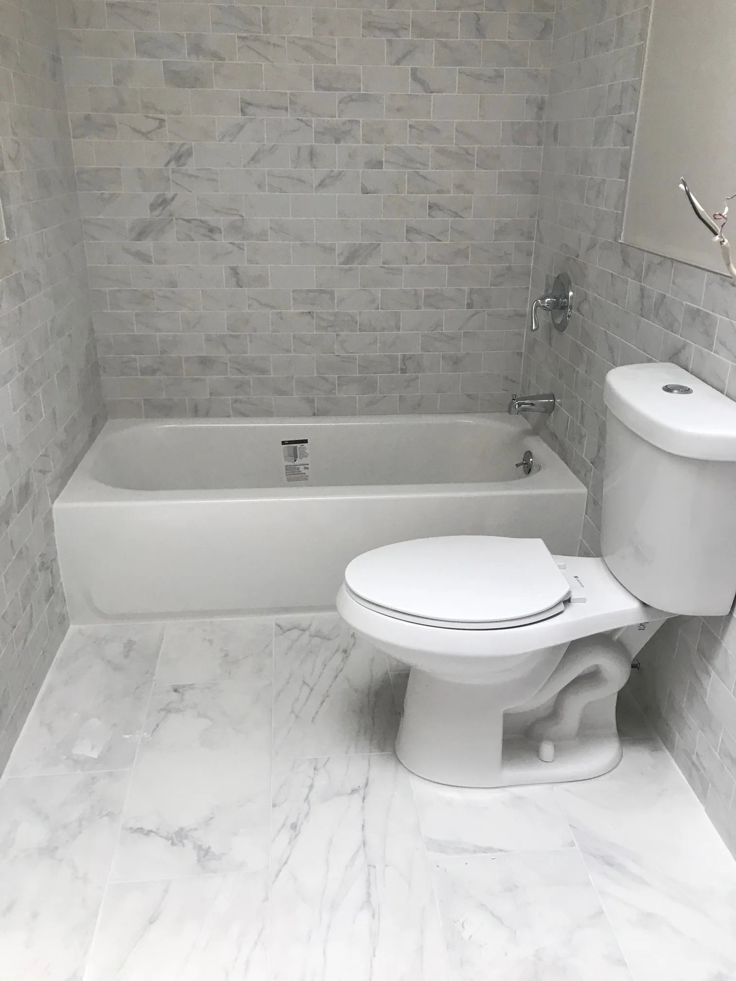 Bathroom with marble flooring, gray subway tile walls, white tub and toilet fixtures