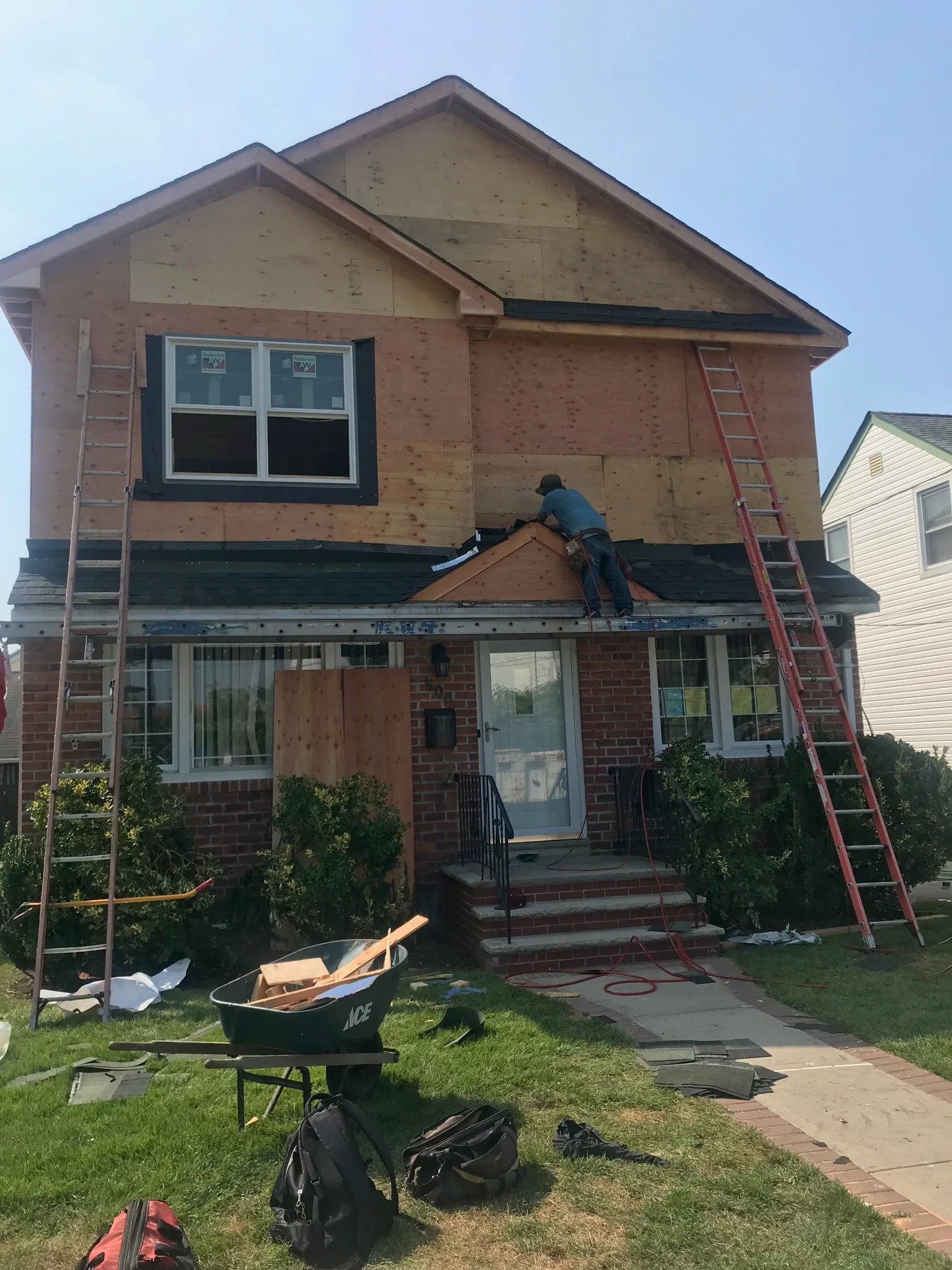 Brick home with exposed roof framing, new plywood sheathing, and worker installing roofing materials