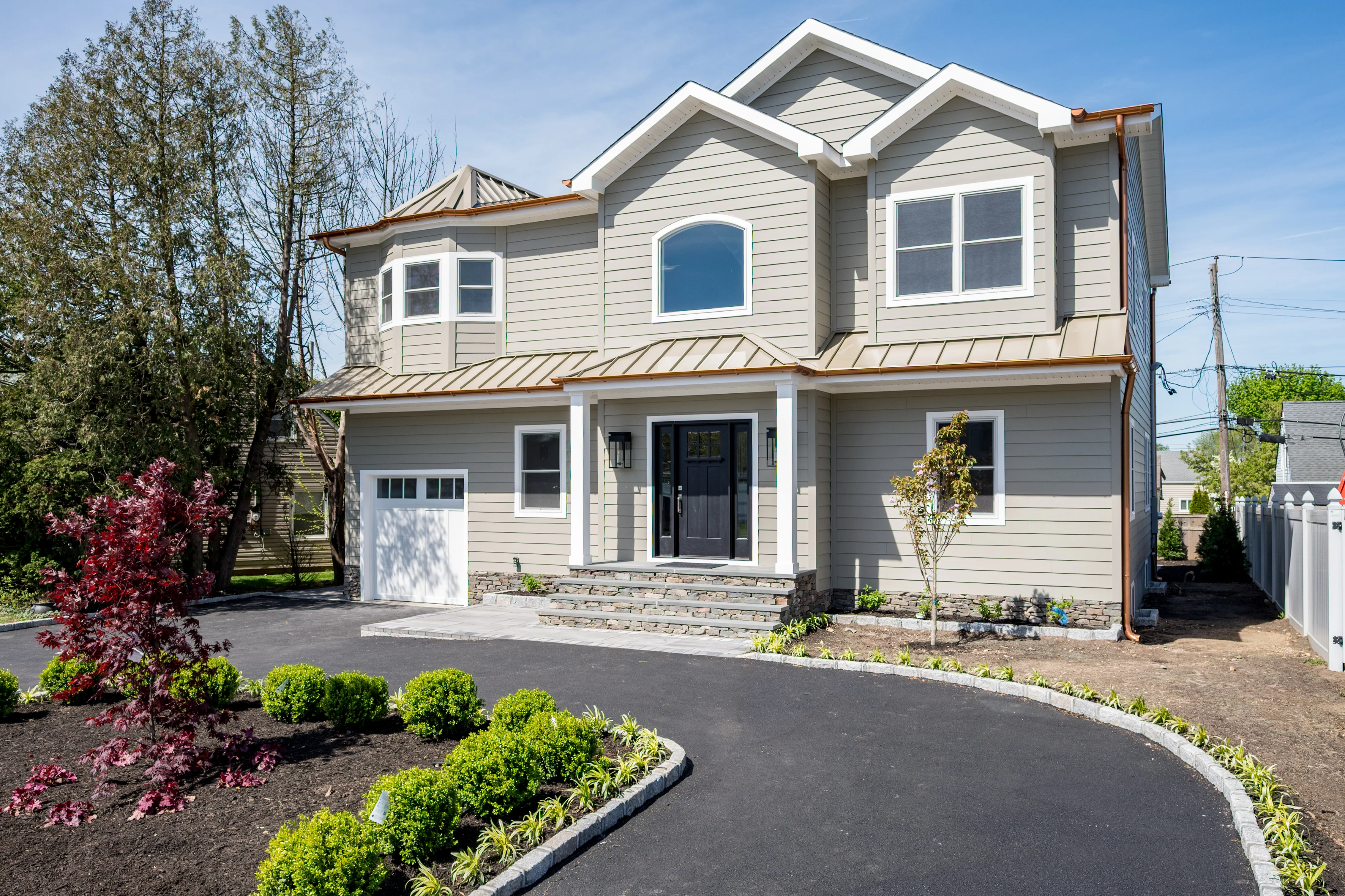 Two-story home with gray siding, metal roof, white garage door, and stone foundation base