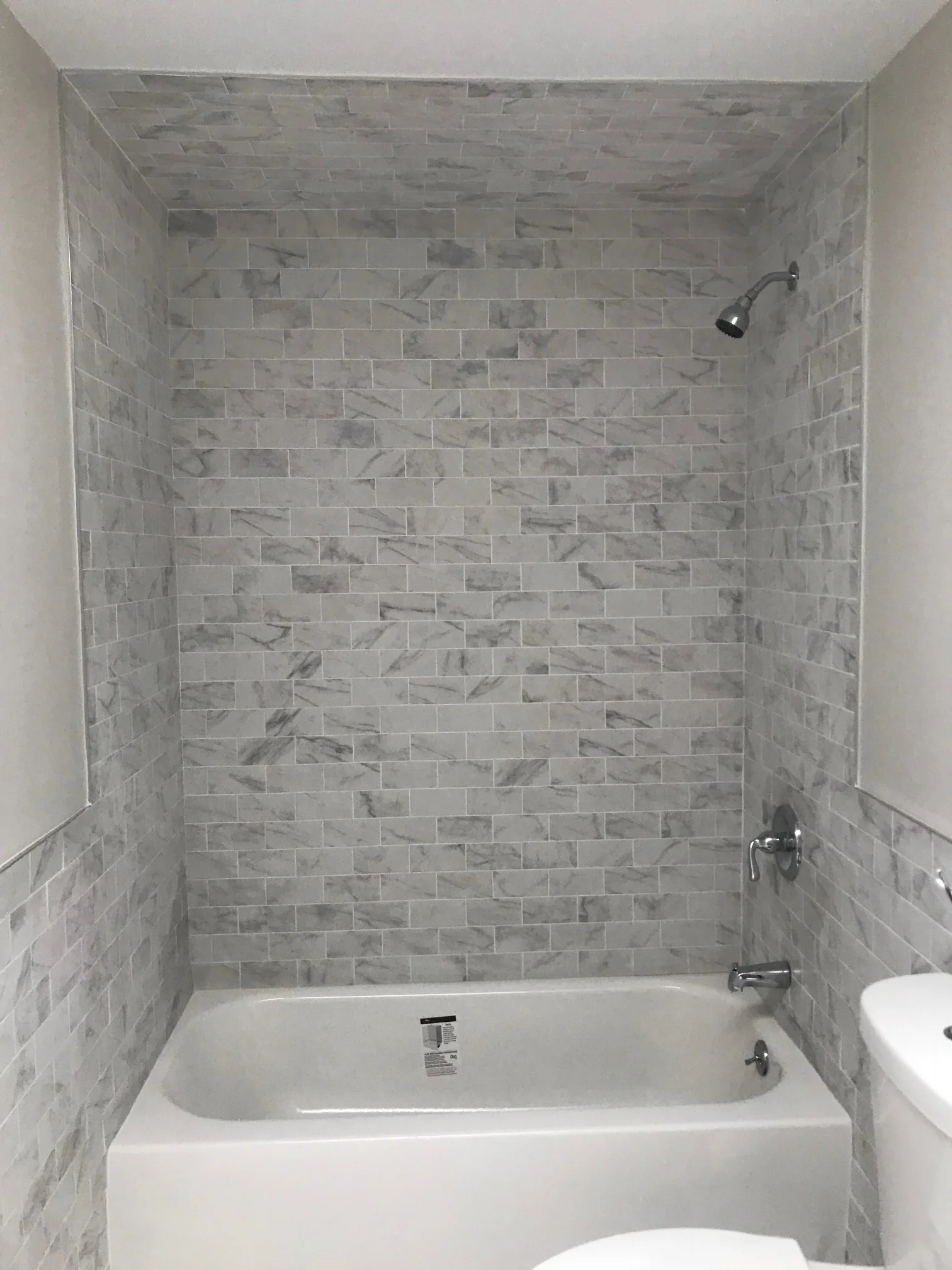 Marble subway tile bathroom surround with white bathtub and chrome fixtures