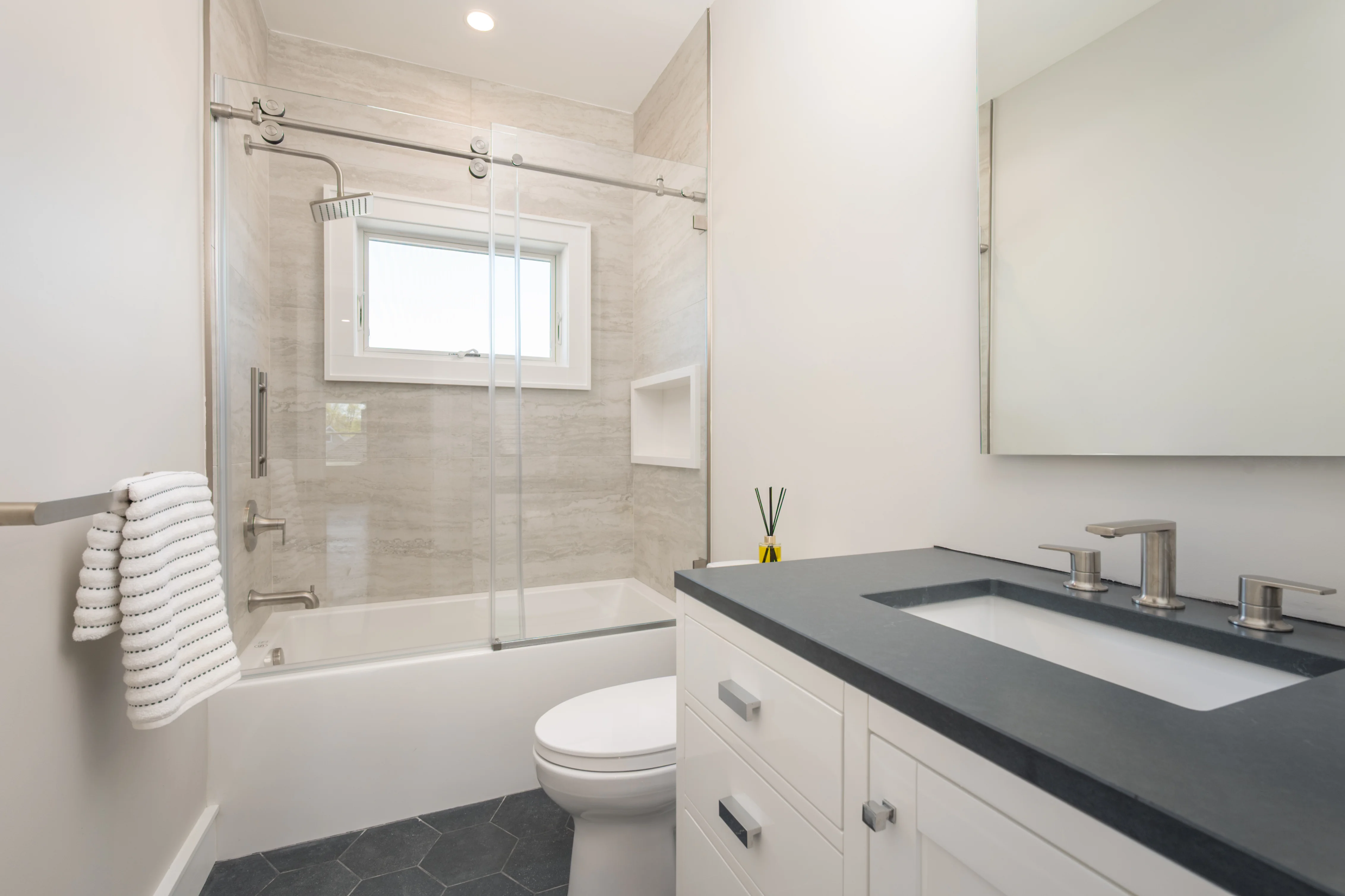 Modern bathroom with frameless glass shower, white cabinetry, black quartz countertop, and gray tile flooring