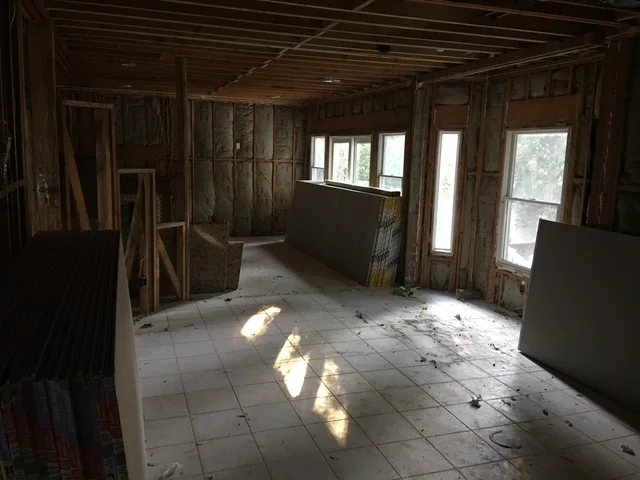 Interior demolition showing exposed framing, removed drywall, and tile flooring with windows