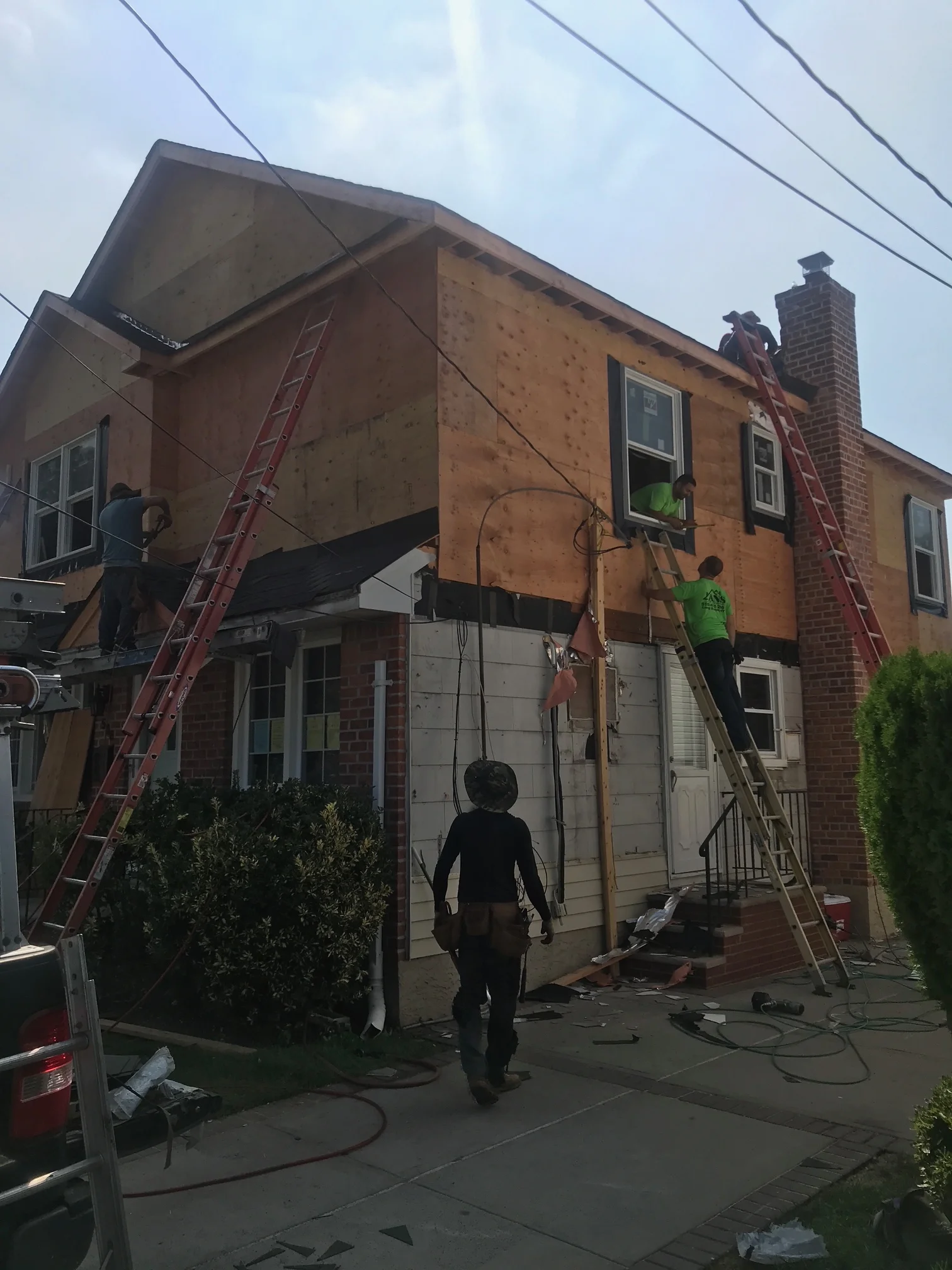 Brick home with charred exterior, workers on ladders removing damaged materials and siding