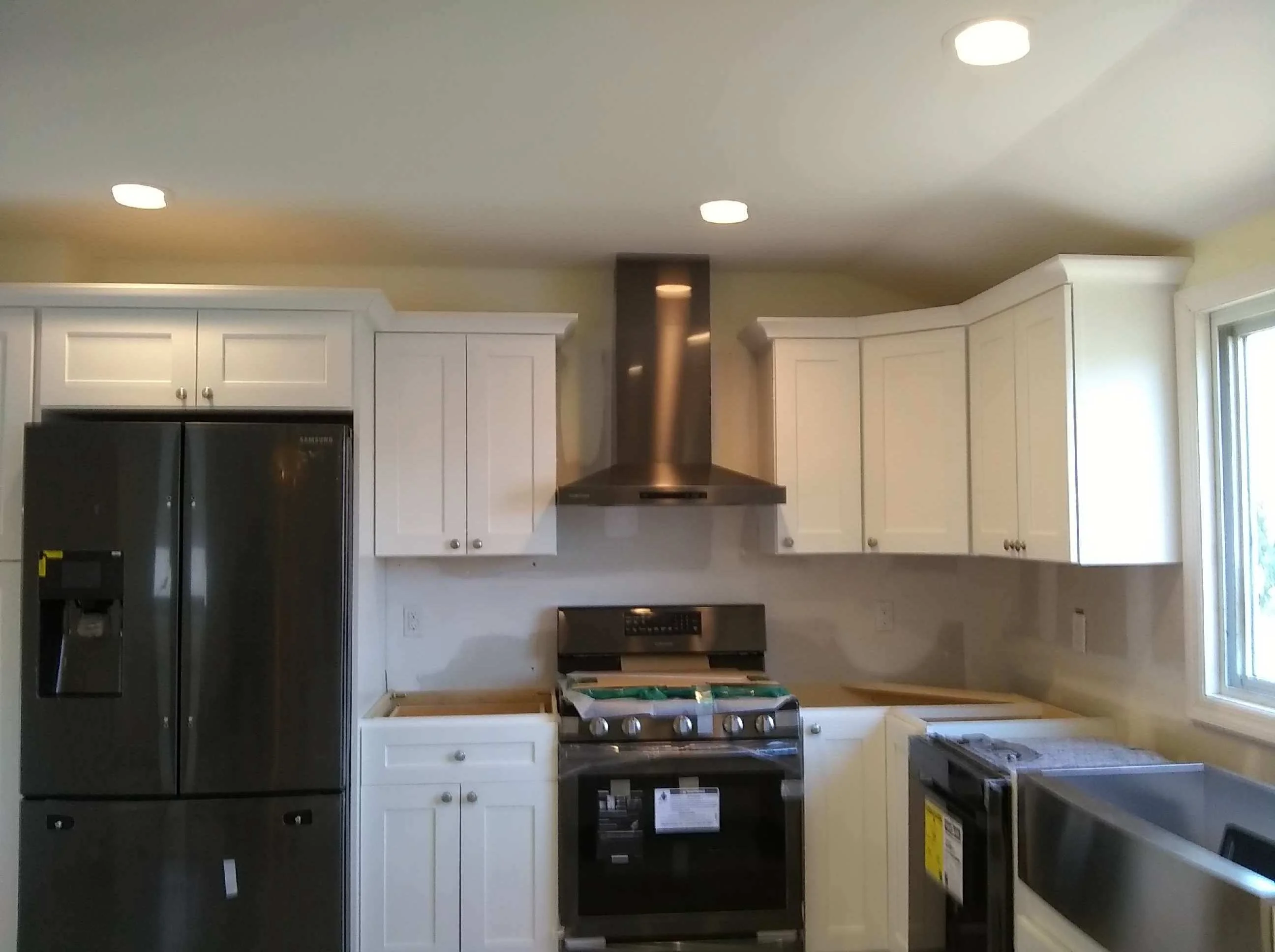 White cabinetry kitchen with black stainless appliances, bronze range hood, and recessed lighting