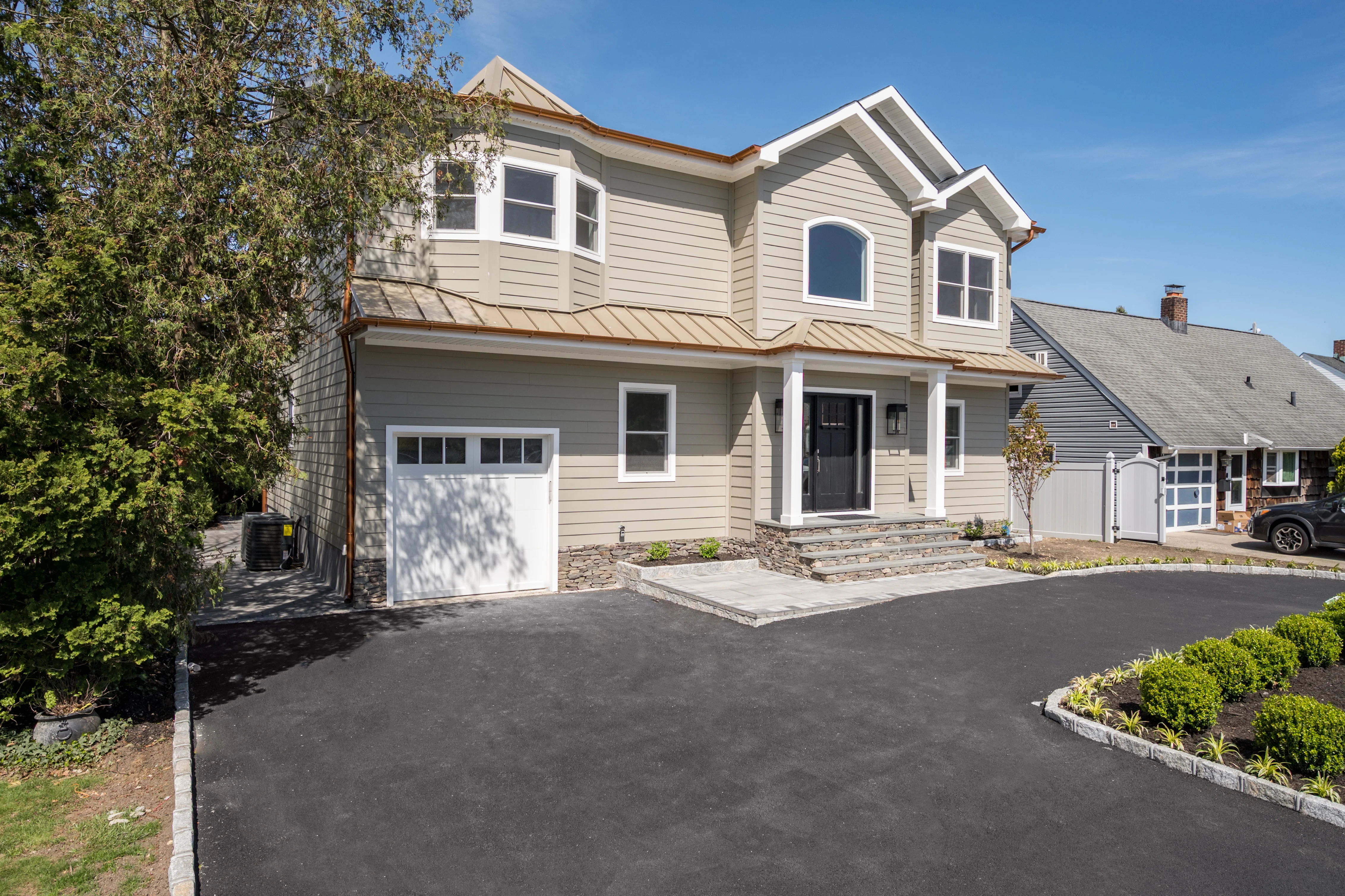 Two-story home with new gray siding, copper roof trim, white garage door, and freshly paved driveway