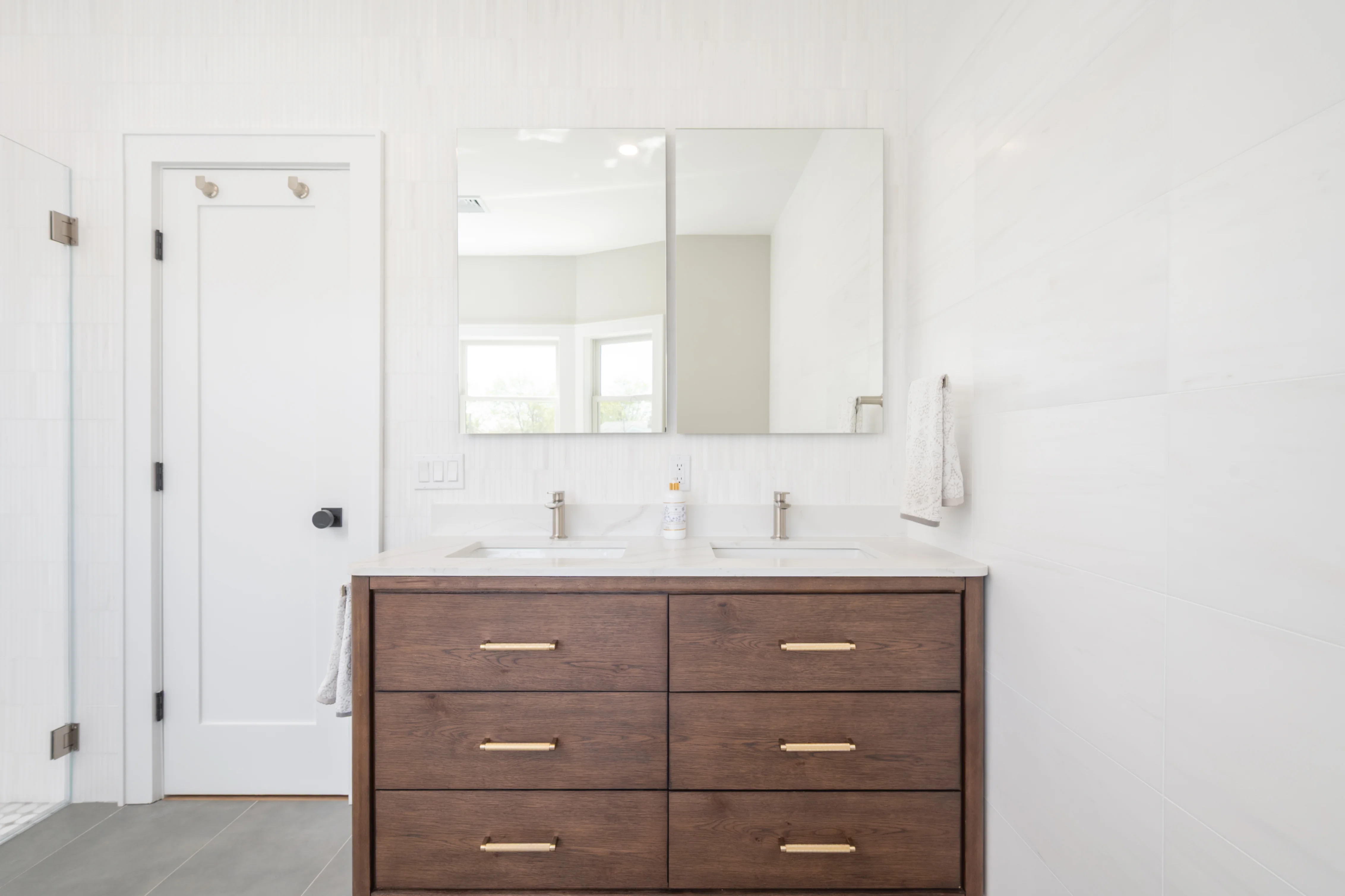 Dark wood double vanity with white quartz top, dual sinks, and large framed mirror in white bathroom